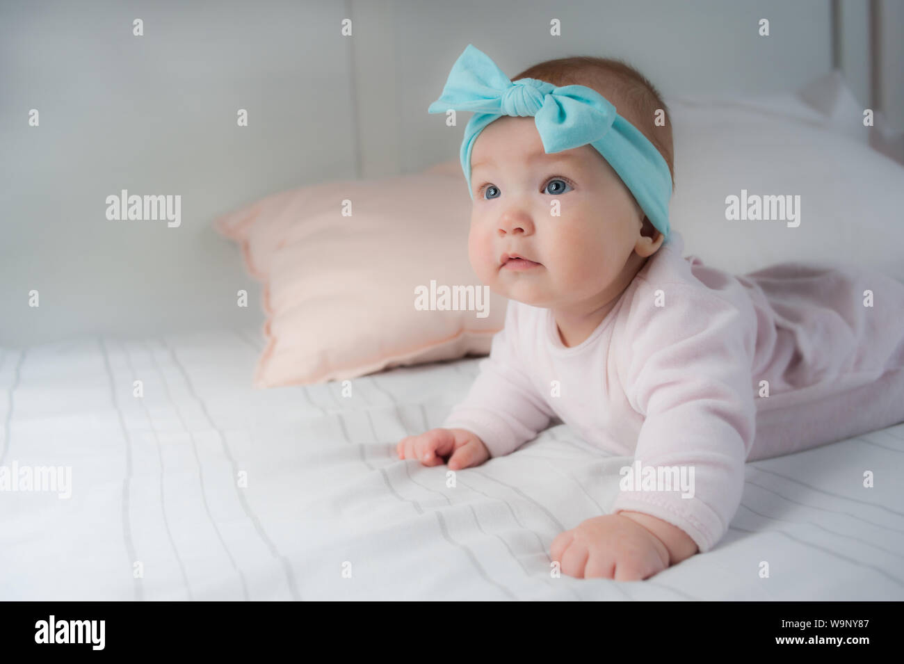 Newborn child wearing a diaper in white sunny bedroom. Newborn child relaxing in bed. Beautiful girl lies a happy smile, great design for any purposes Stock Photo