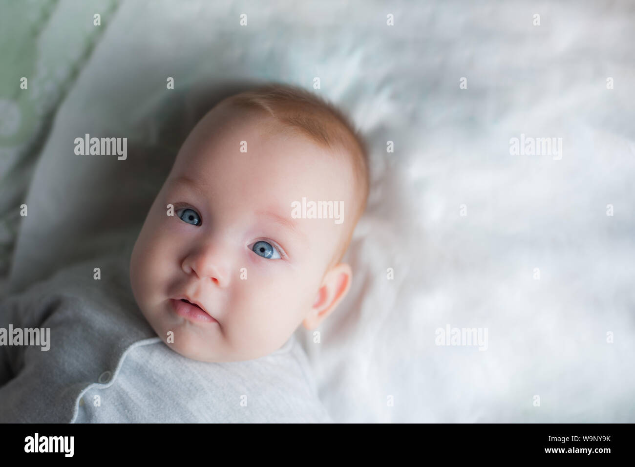 Newborn child wearing a diaper in white sunny bedroom. Newborn child relaxing in bed. Beautiful girl lies a happy smile, great design for any purposes Stock Photo