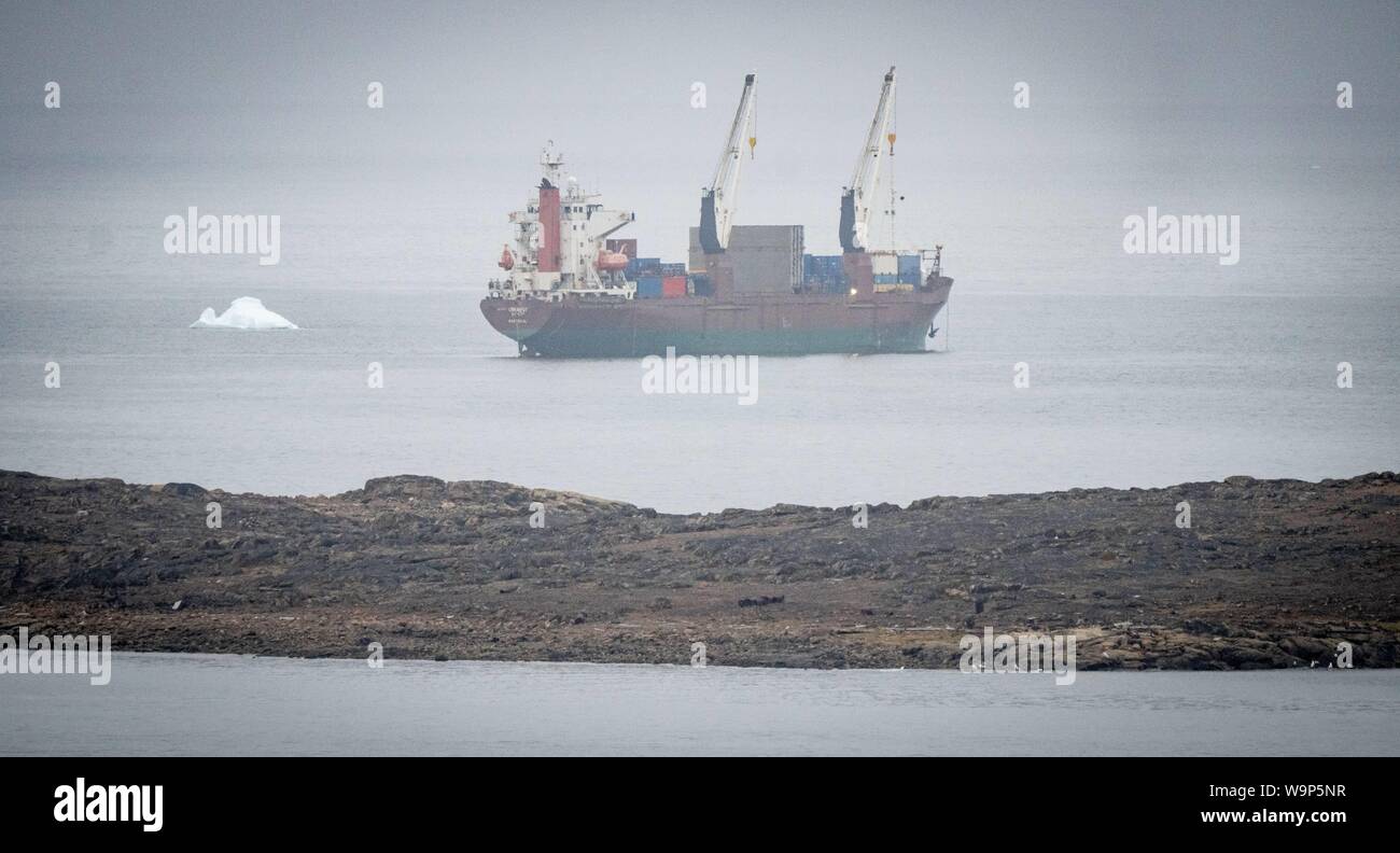 Iqaluit, Canada. 14th Aug, 2019. A freighter anchors off the city of Iqaluit in northern Canada next to an iceberg. German Foreign Minister Maas is visiting the Arctic region to get an idea of the extent of climate change. Credit: Kay Nietfeld/dpa/Alamy Live News Stock Photo