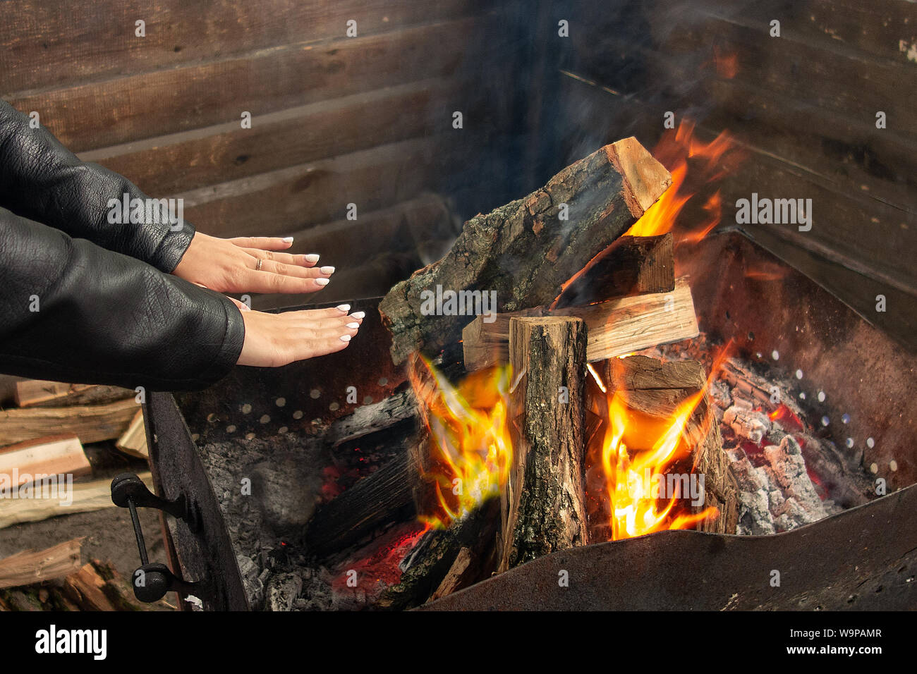 Girl warms up near open fire. Woman holds hands above flame to toast