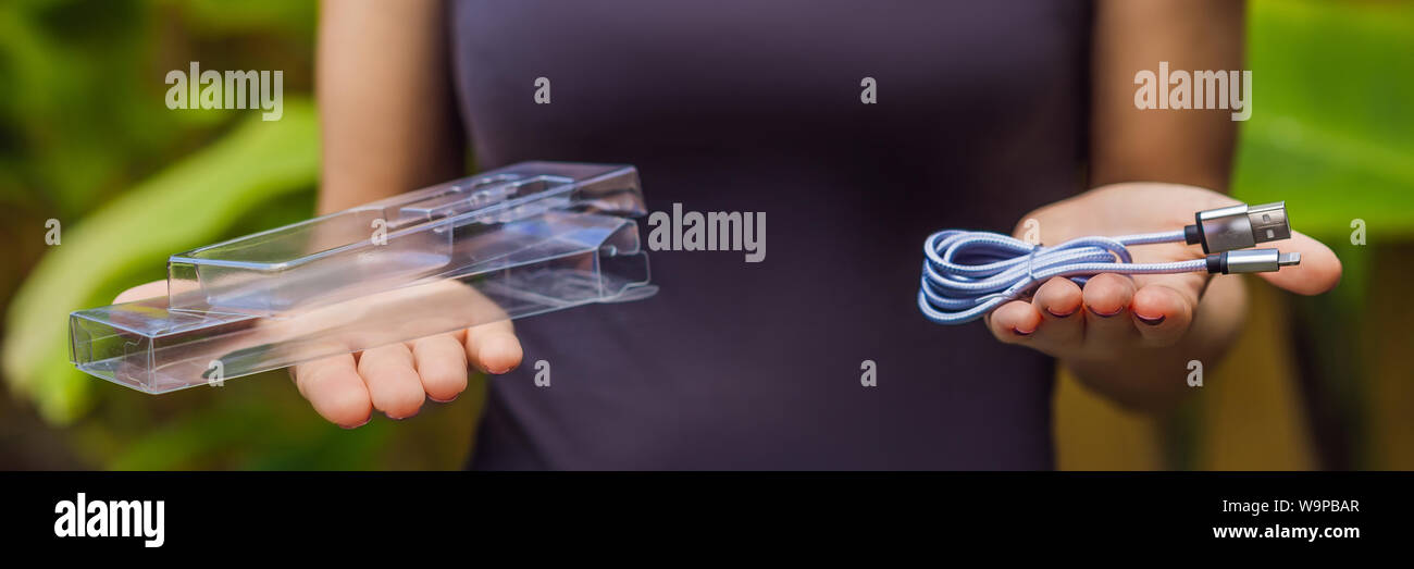 Female hands printed a new wire to charge the phone. The wire was packed in a large number of plastic packaging, which will be thrown into the trash Stock Photo