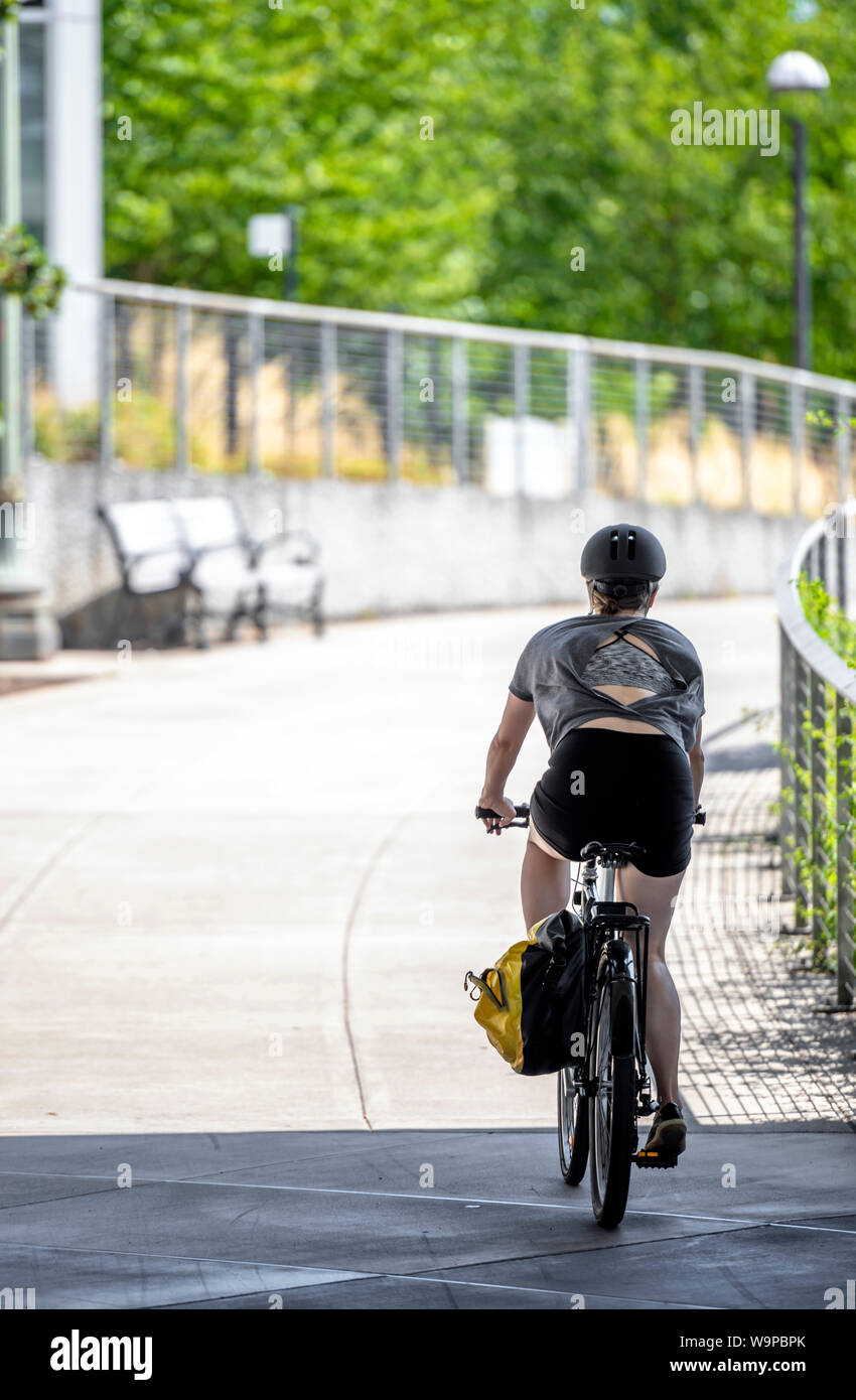 A woman cyclist in sportswear running on the sidewalk on a bicycle, preferring an active way of relaxation, helping her to keep herself in good shape, Stock Photo