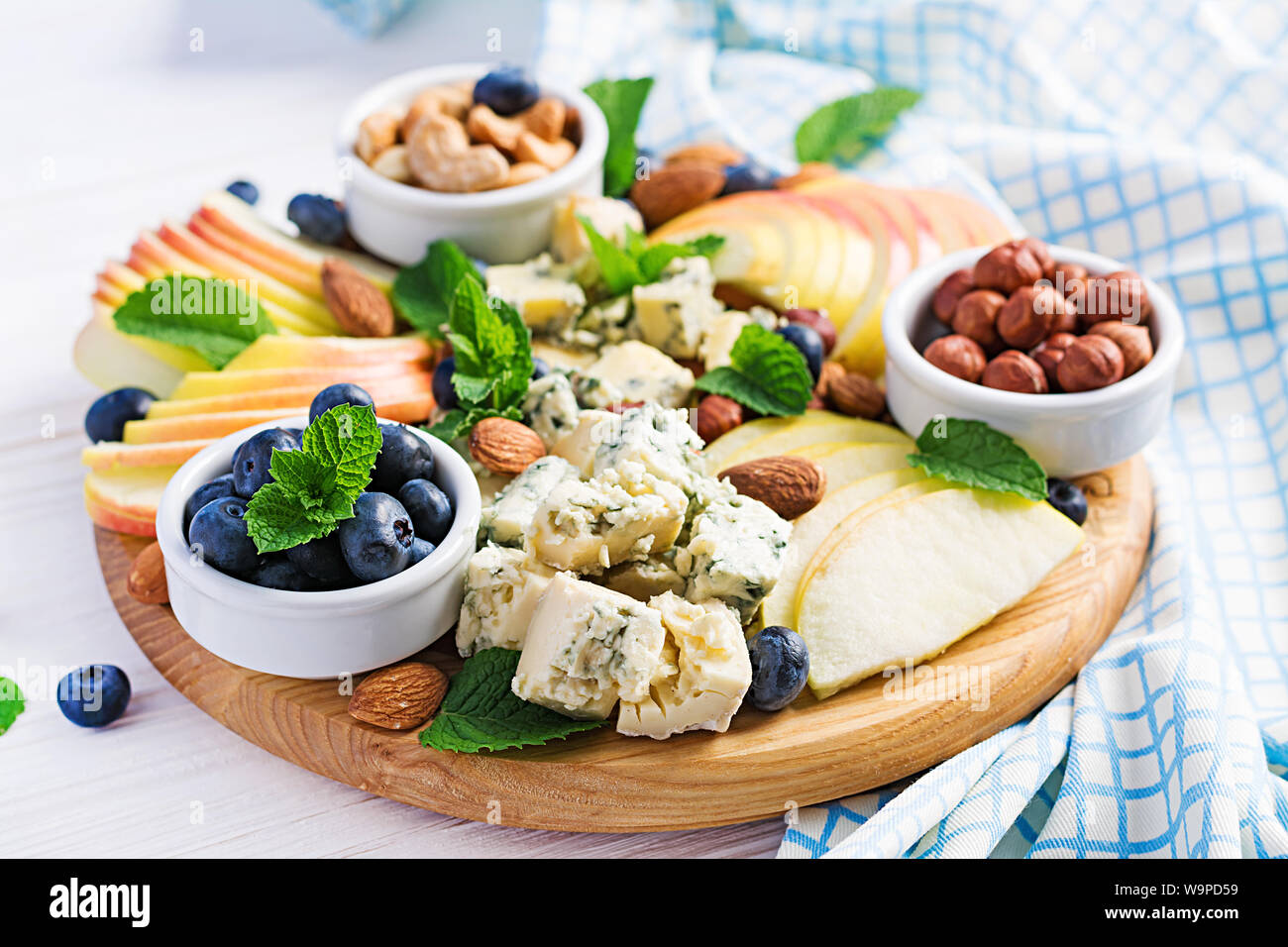 Cheese platter with assorted cheeses, blueberry, apples, nuts on white