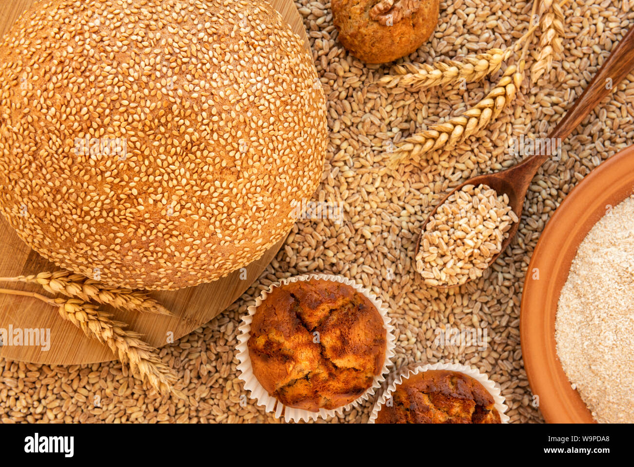 Still life of bread, muffins, cookies, spikelets, a plate of spelt flour and a spoon filled with grains.  It is against the background of scattered gr Stock Photo