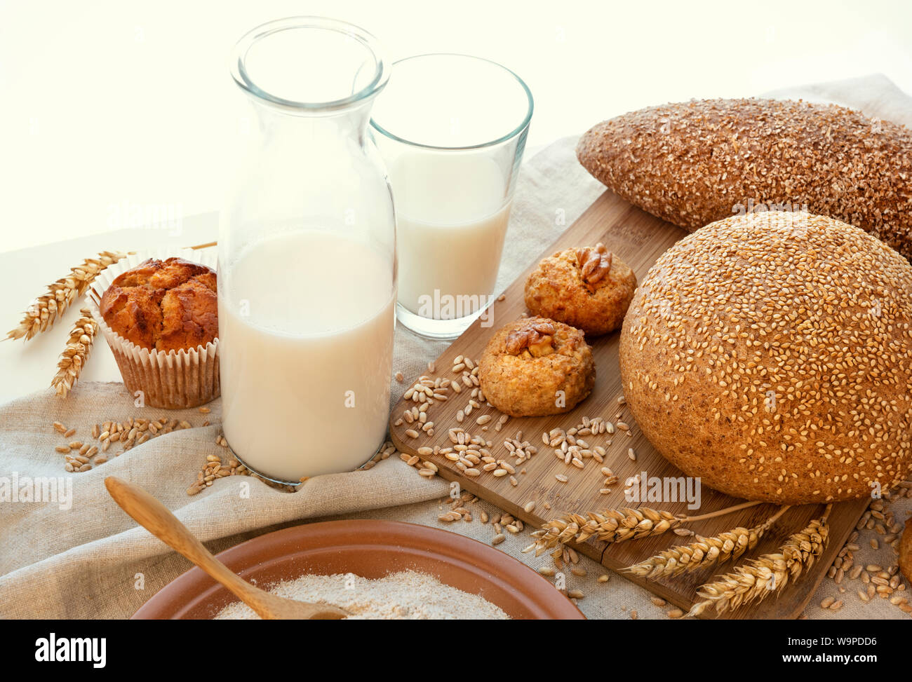 Still life of milk, breads, cupcake, biscuits, a plate of bran, spikelets of spelled and scattered poldba grains.  It is all on hemp cloth and on a wh Stock Photo