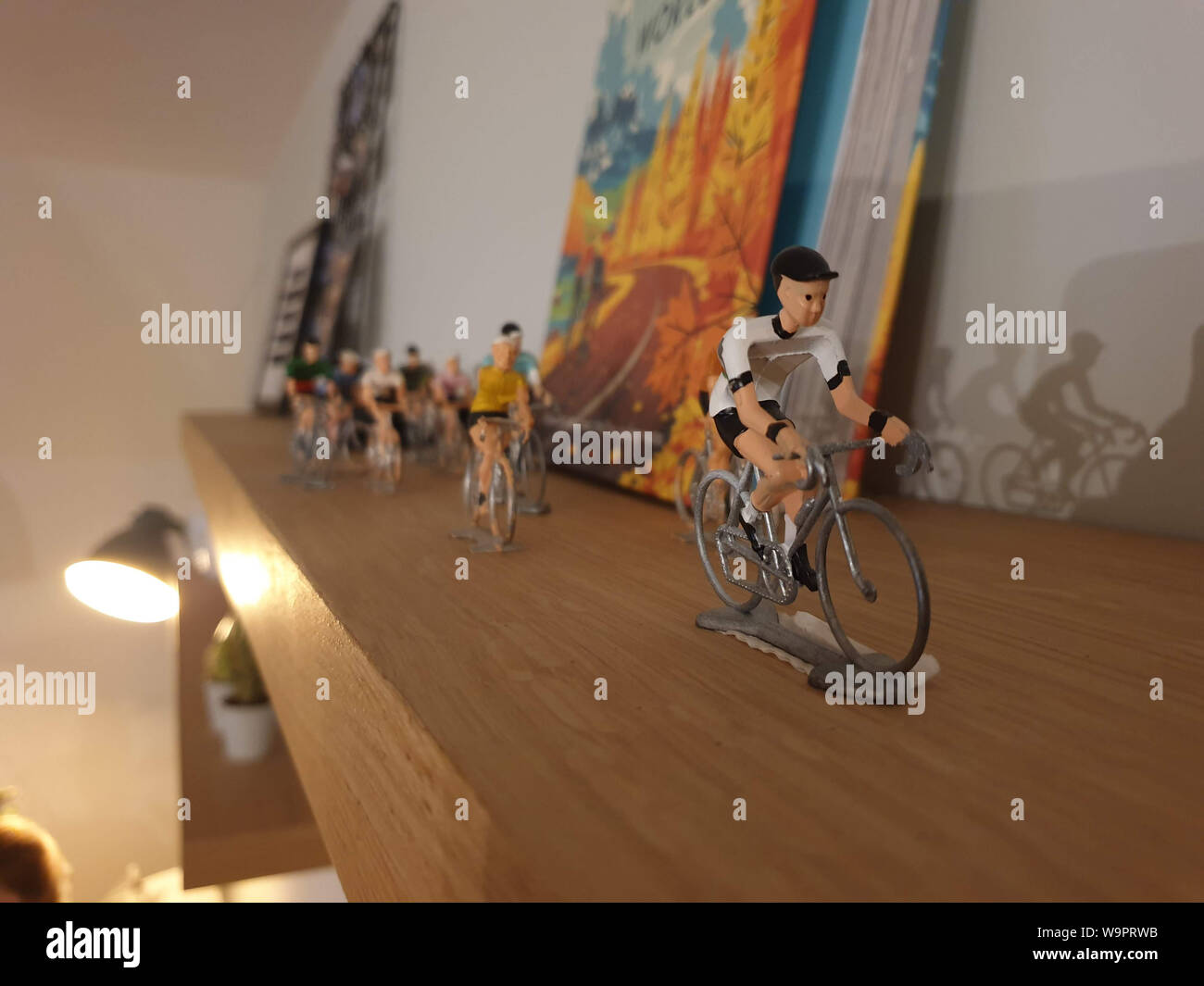 A portrait of miniaturen cyclists riding their bikes on a wooden bookshelf in an indoor environment. One of the toys is in the lead and the rest are f Stock Photo