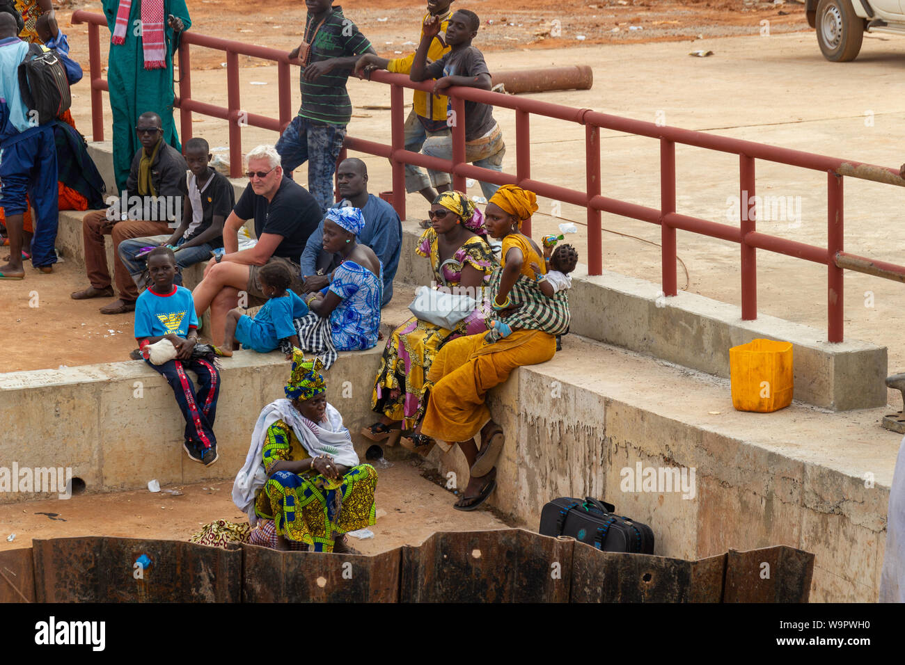 YELITENDA, GAMBIA- JAN 6, 2014: No bridge across the Gambia River. Everyone has to wait for their turn. Women waiting in colorful dresses. Stock Photo