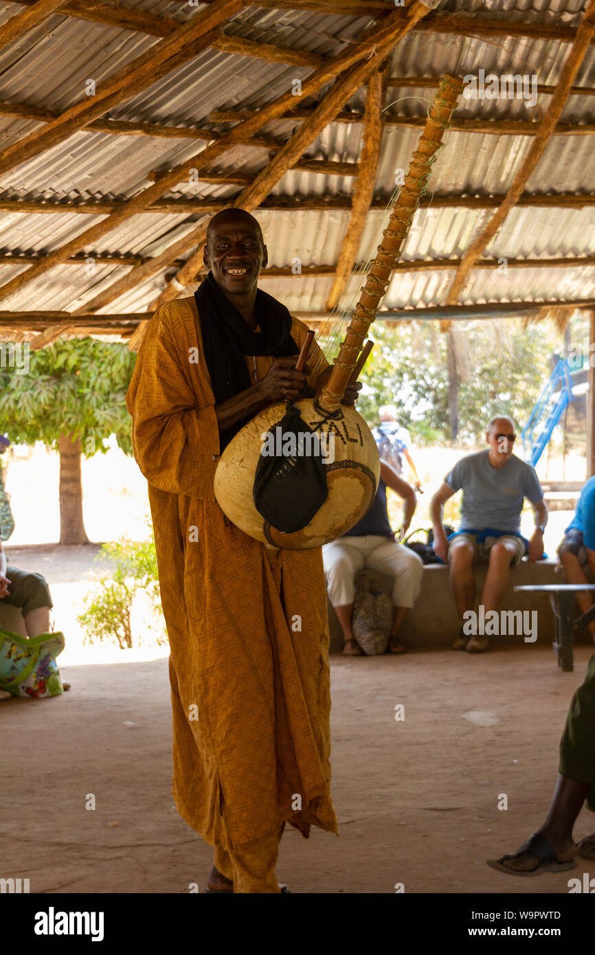 JUFUREH, GAMBIA- JAN 12, 2014: The Kora is a Mandinka instument build from a calebash. He walks around smiling, while playing the instrument Stock Photo