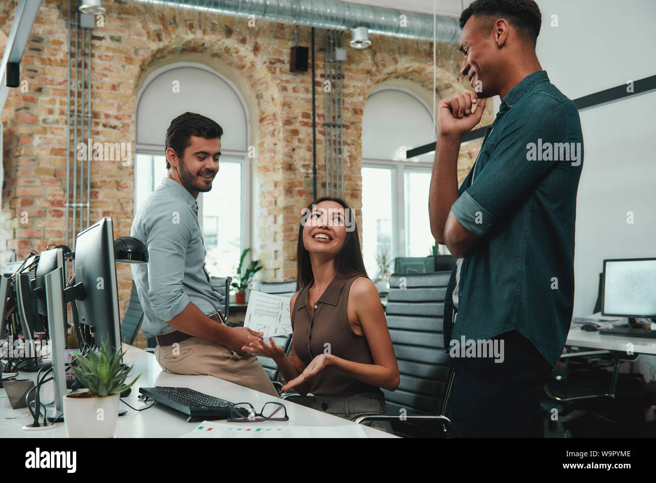 We are happy to work together. Group of cheerful young business people in casual wear are talking and smiling while working in modern office. Cooperation. Workplace Stock Photo