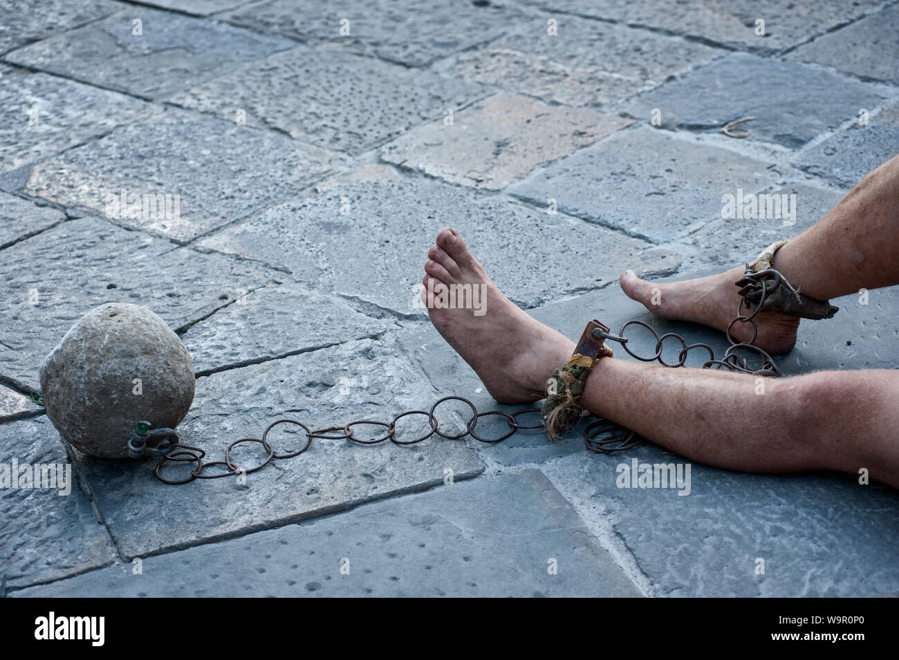Prisioner with ball and chain in the court of the prison. Close up. Concept of inhuman and degrading detention conditions. Stock Photo