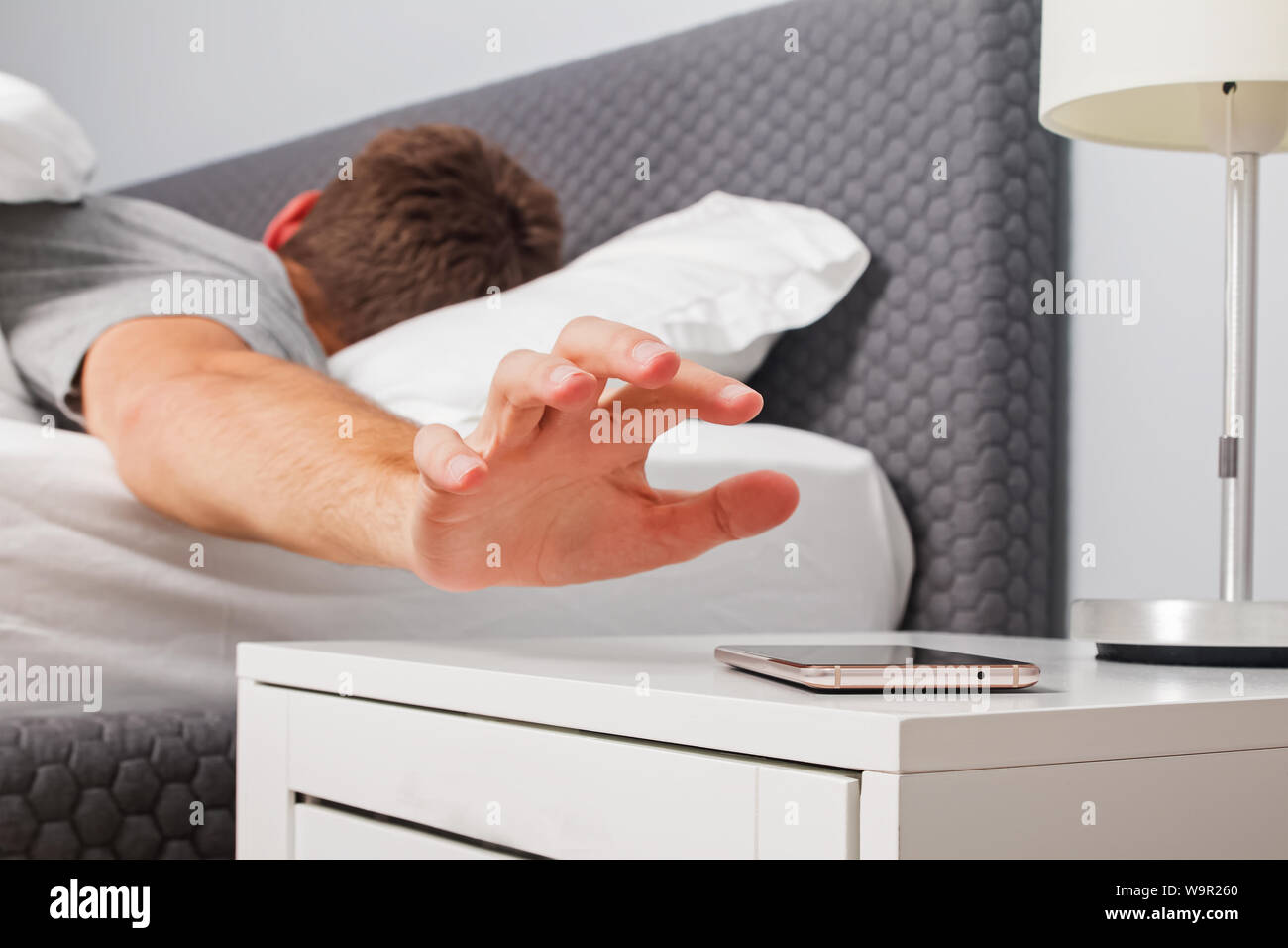 Man's hand close-up trying to reach out ringing cell phone or alarm to have some snooze early in the morning. Stock Photo