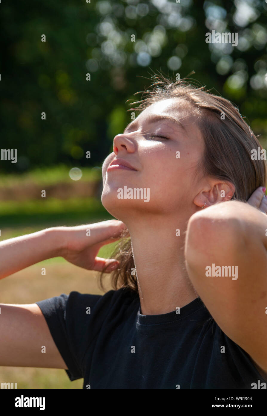 Tennage girl dressed in black sits on grass pulls back hair face to sun Stock Photo
