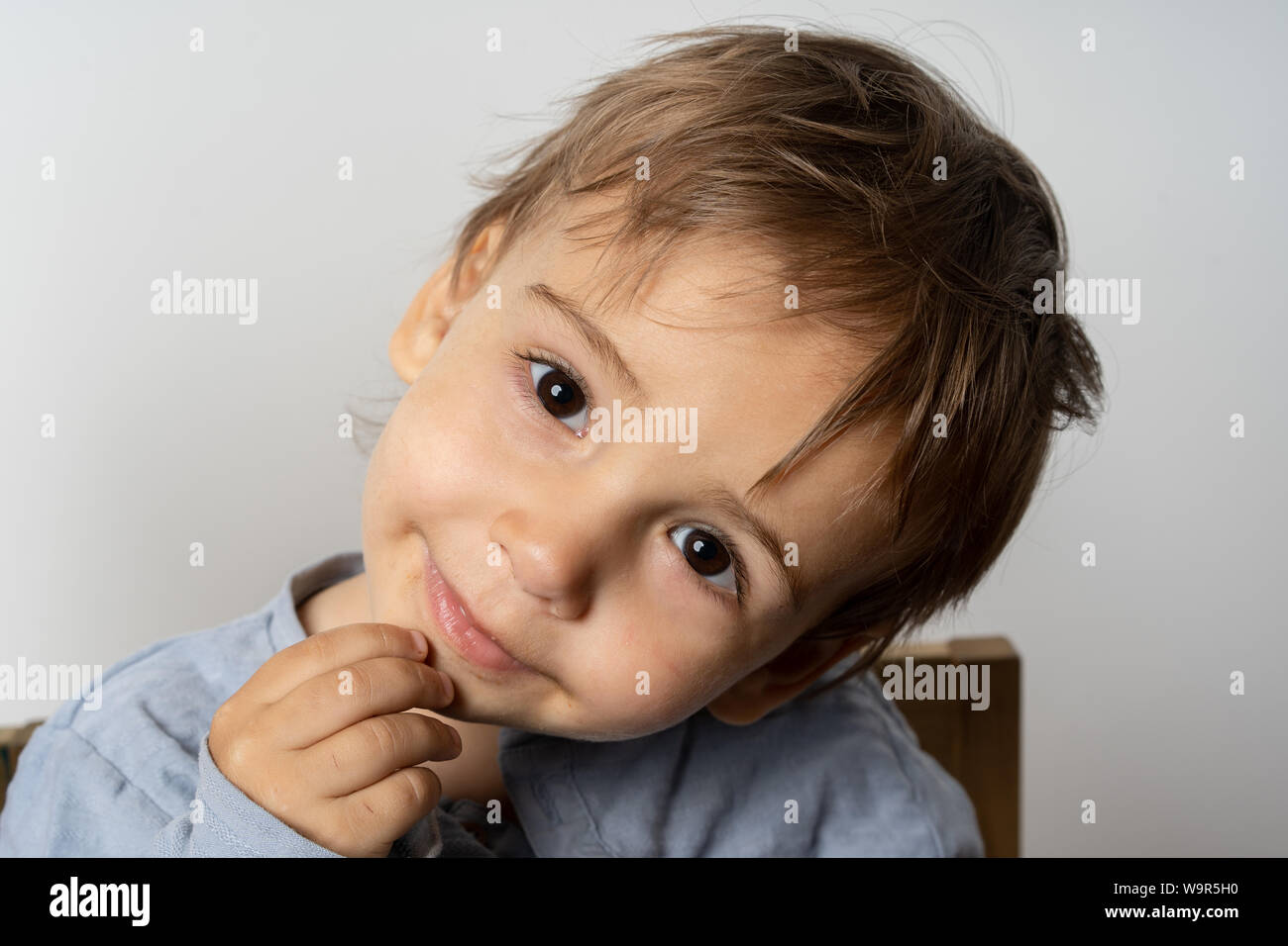 Attractive little boy 5-7 years old in a white jacket is smiling on a white background. Super cute caucasian young boy. Stock Photo