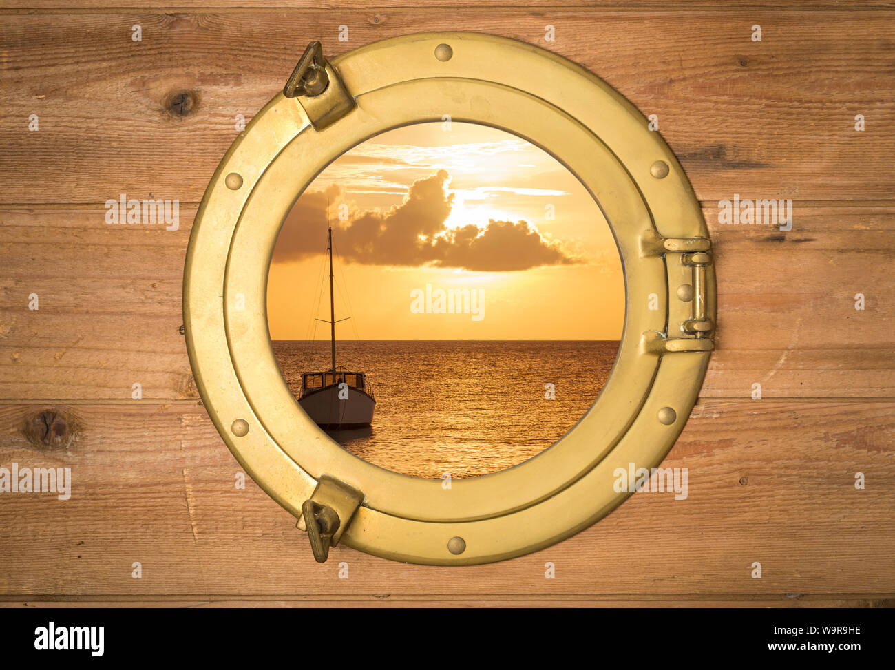 Vintage brass porthole in rustic wooden wall with view to a boat in sunset Stock Photo