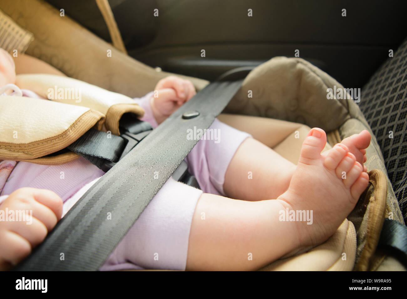 Safety concept, protection of child in travel, children feet in baby seat. Small newborn baby sitting in special car seat with safety seatbelts Stock Photo