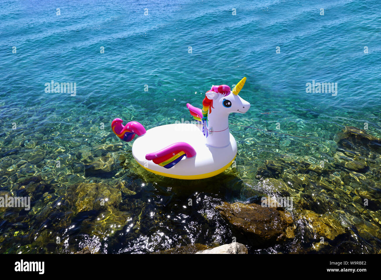 Mandre, Croatia, August 11, 2019. Summer, holiday and vacation background with copy space. Inflatable unicorn in the shallow blue sea water on the sun Stock Photo
