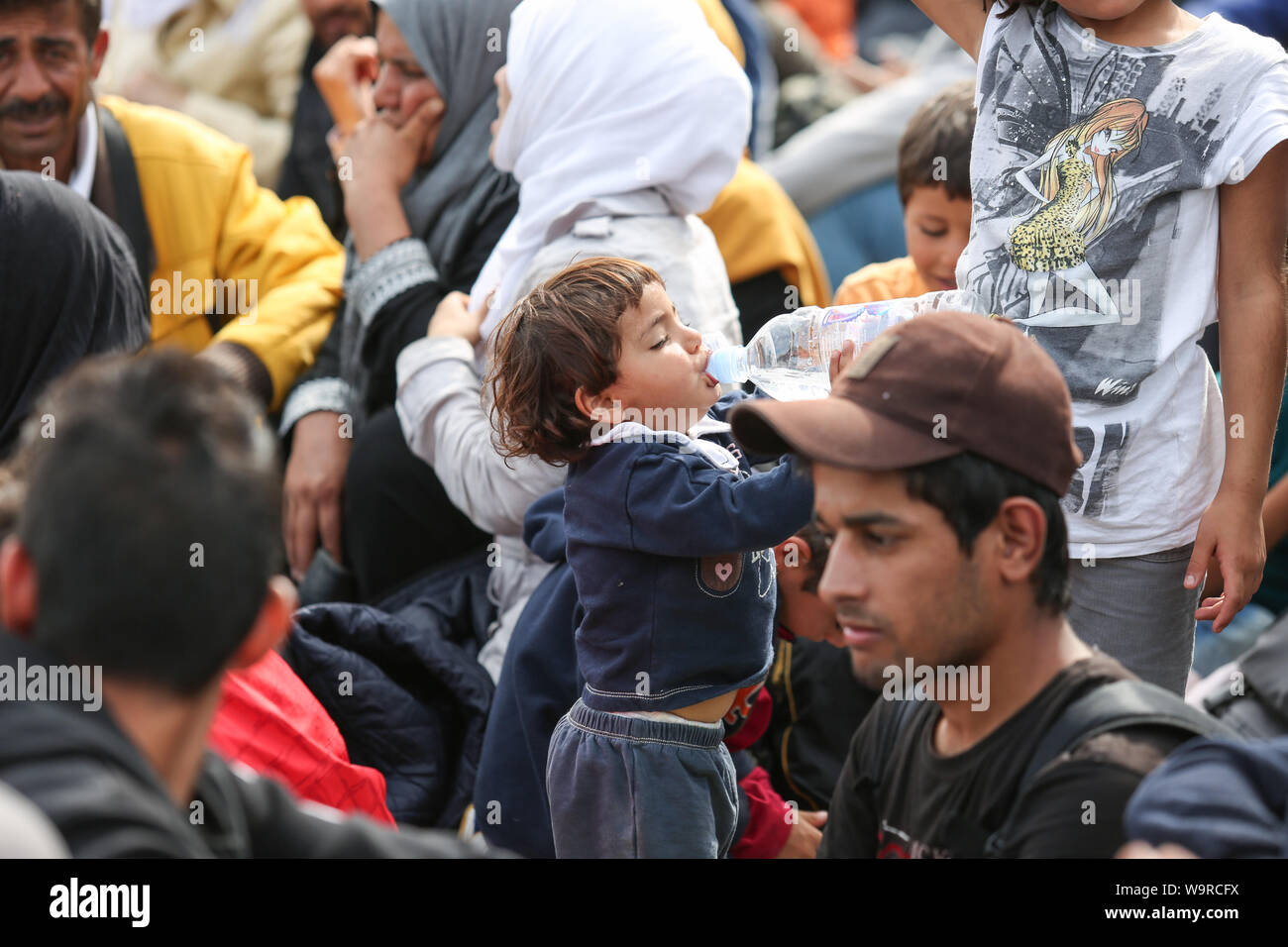 Bregana, Slovenia - September 20, 2015 : A small syrian child drinking water out of a bottle among refugees at the slovenian border with Croatia. The Stock Photo
