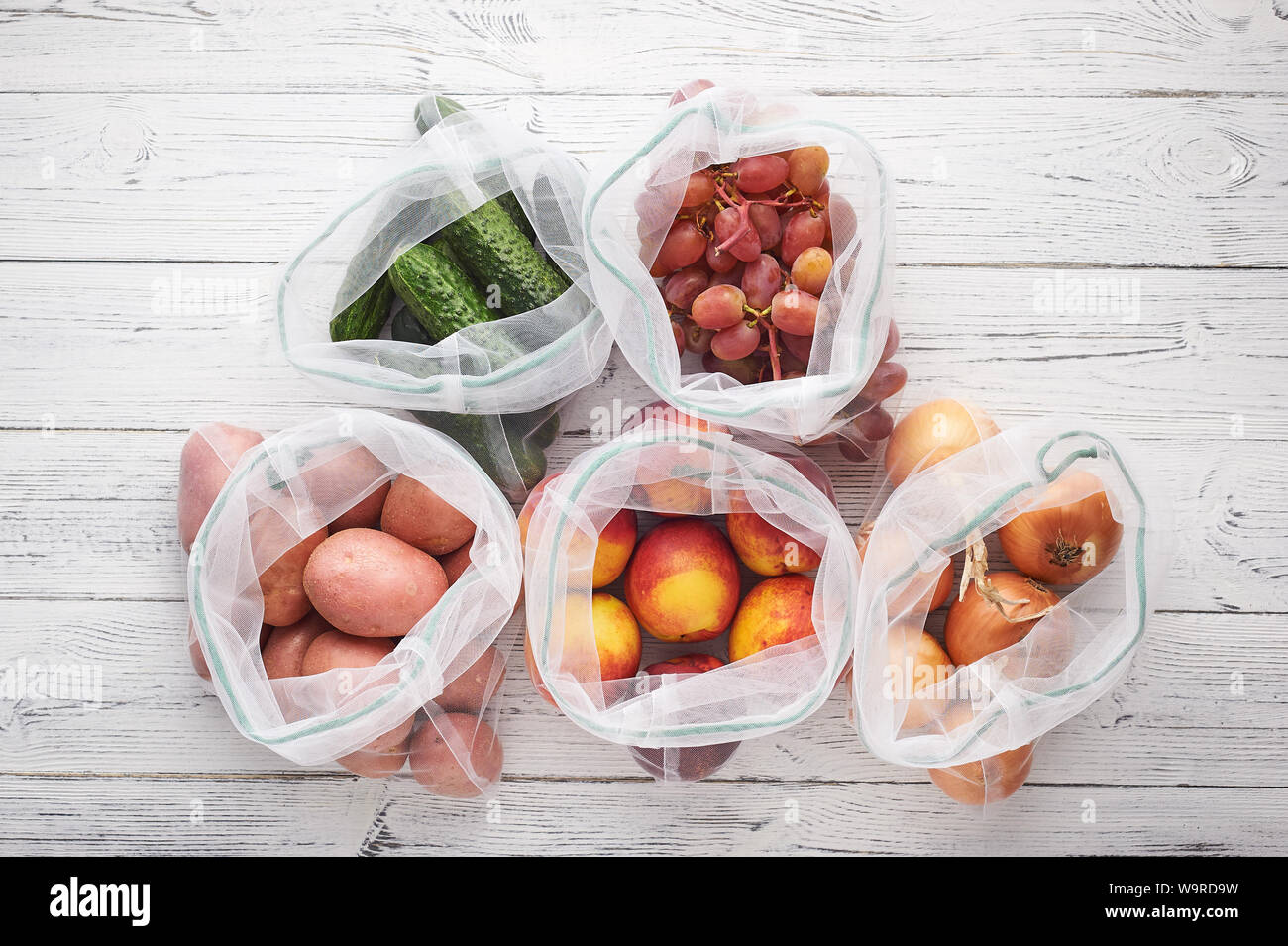 Fruits and vegetables in reusable eco bags at white wooden background ...