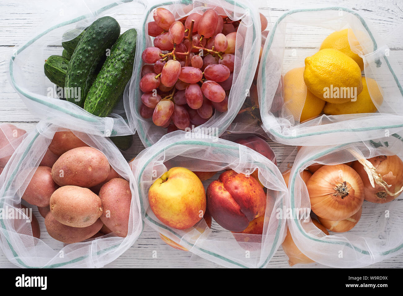 Fruits and vegetables in reusable eco bags at white wooden background