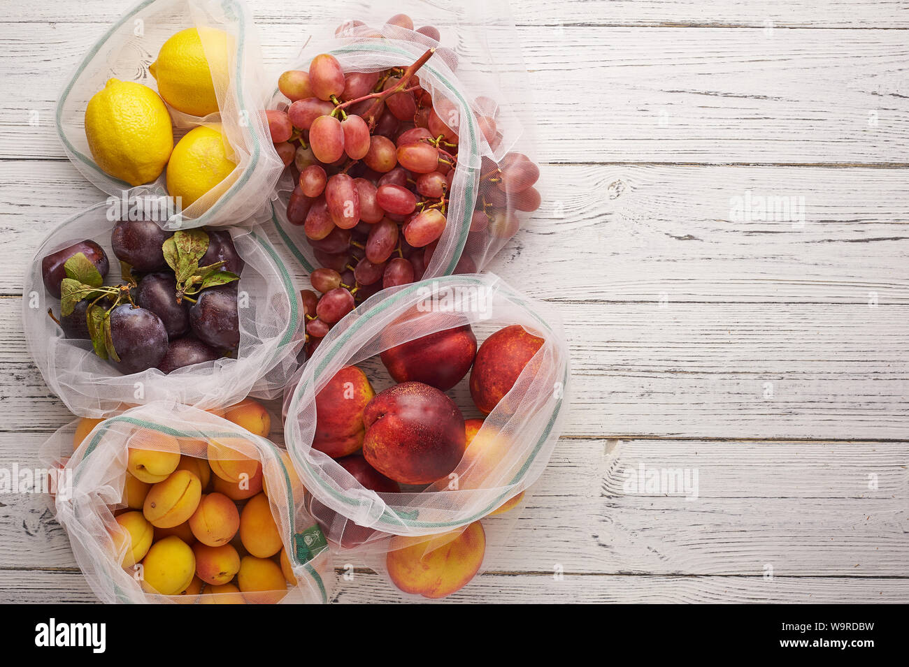 Fruits in reusable eco bags at white wooden background. Recycled bags ...