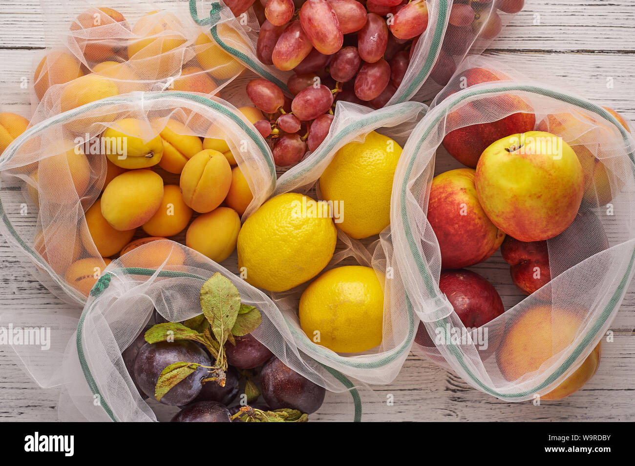 Fruits in reusable eco bags at white wooden background. Recycled bags ...