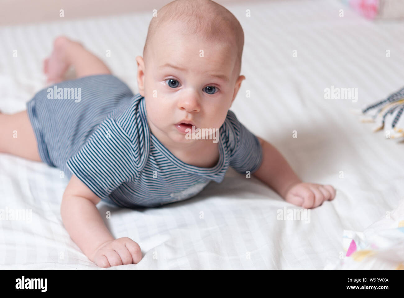 Happy cute four month old baby lying on his stomach on a bed in his