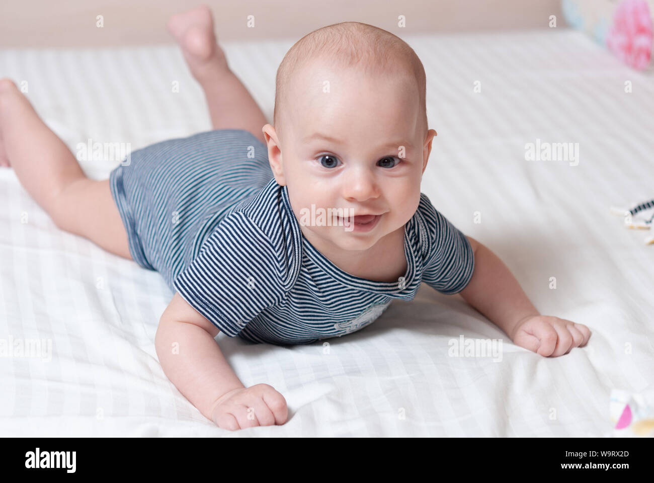 Happy cute four month old baby lying on his stomach on a bed in his