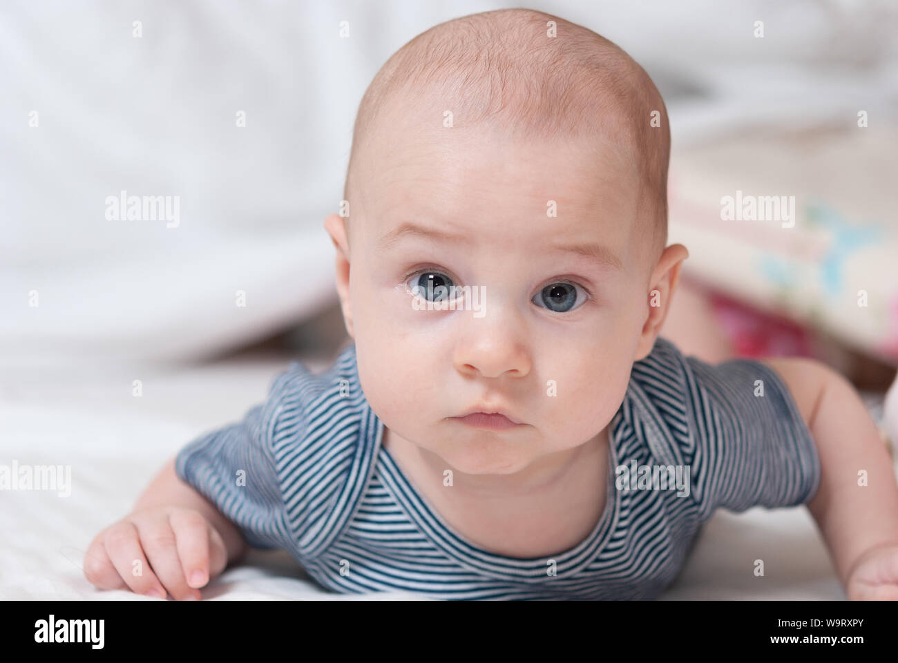 Happy cute four month old baby lying on his stomach on a bed in his