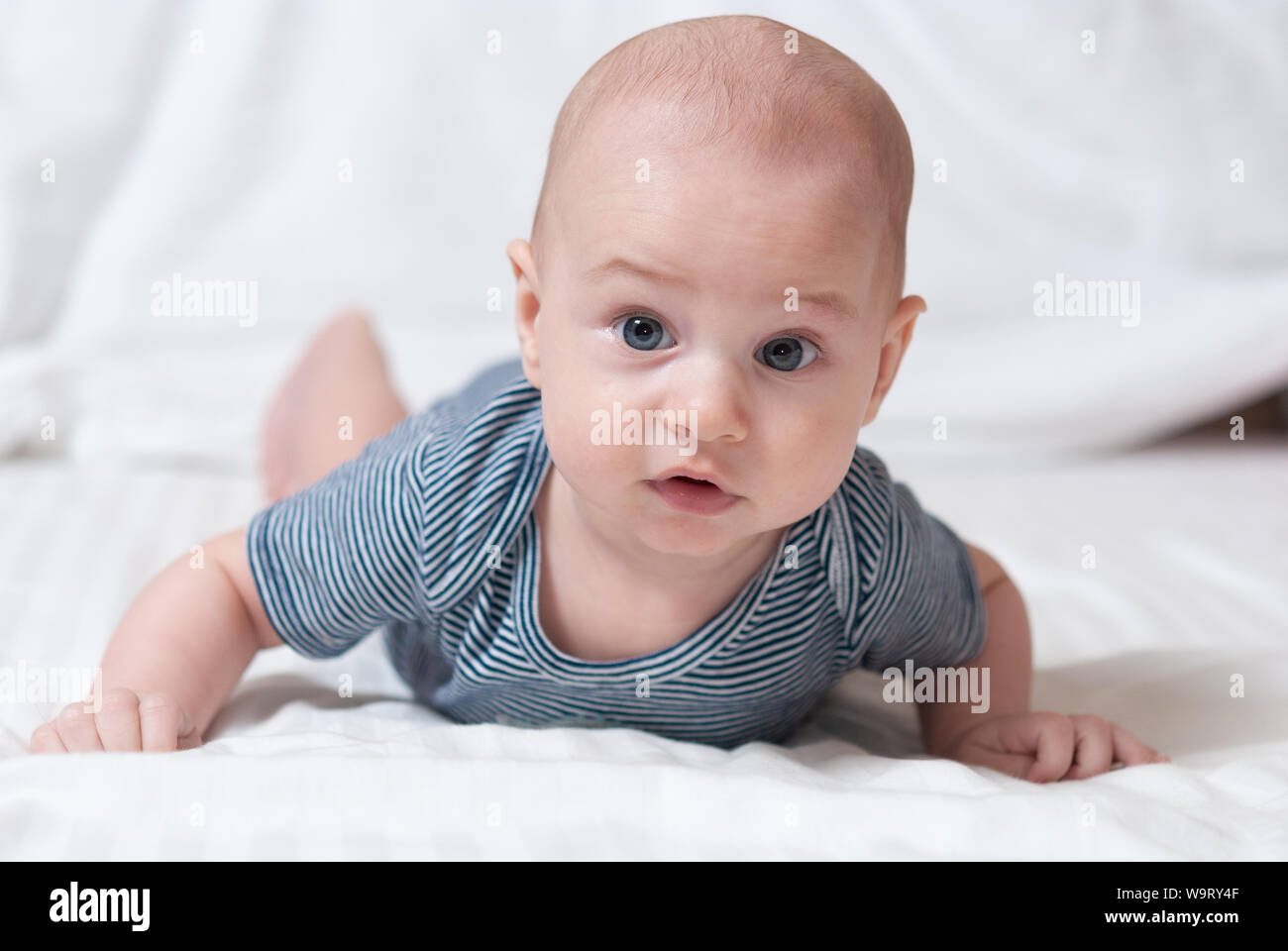 Happy cute four month old baby lying on his stomach on a bed in his
