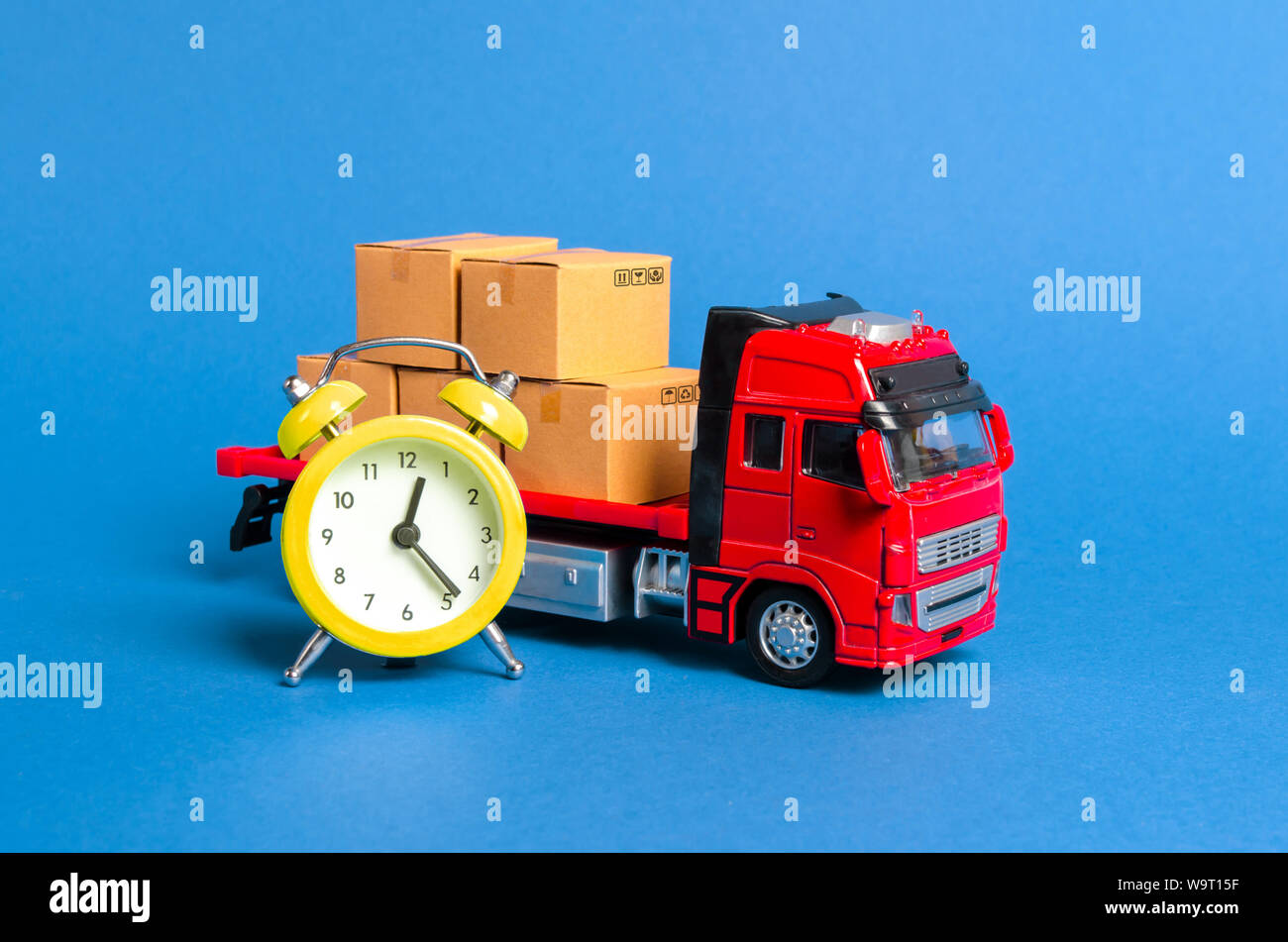 A truck with cargo cardboard boxes and a yellow alarm clock. Express delivery in short time concept. Temporary storage, limited offer and discount. Op Stock Photo