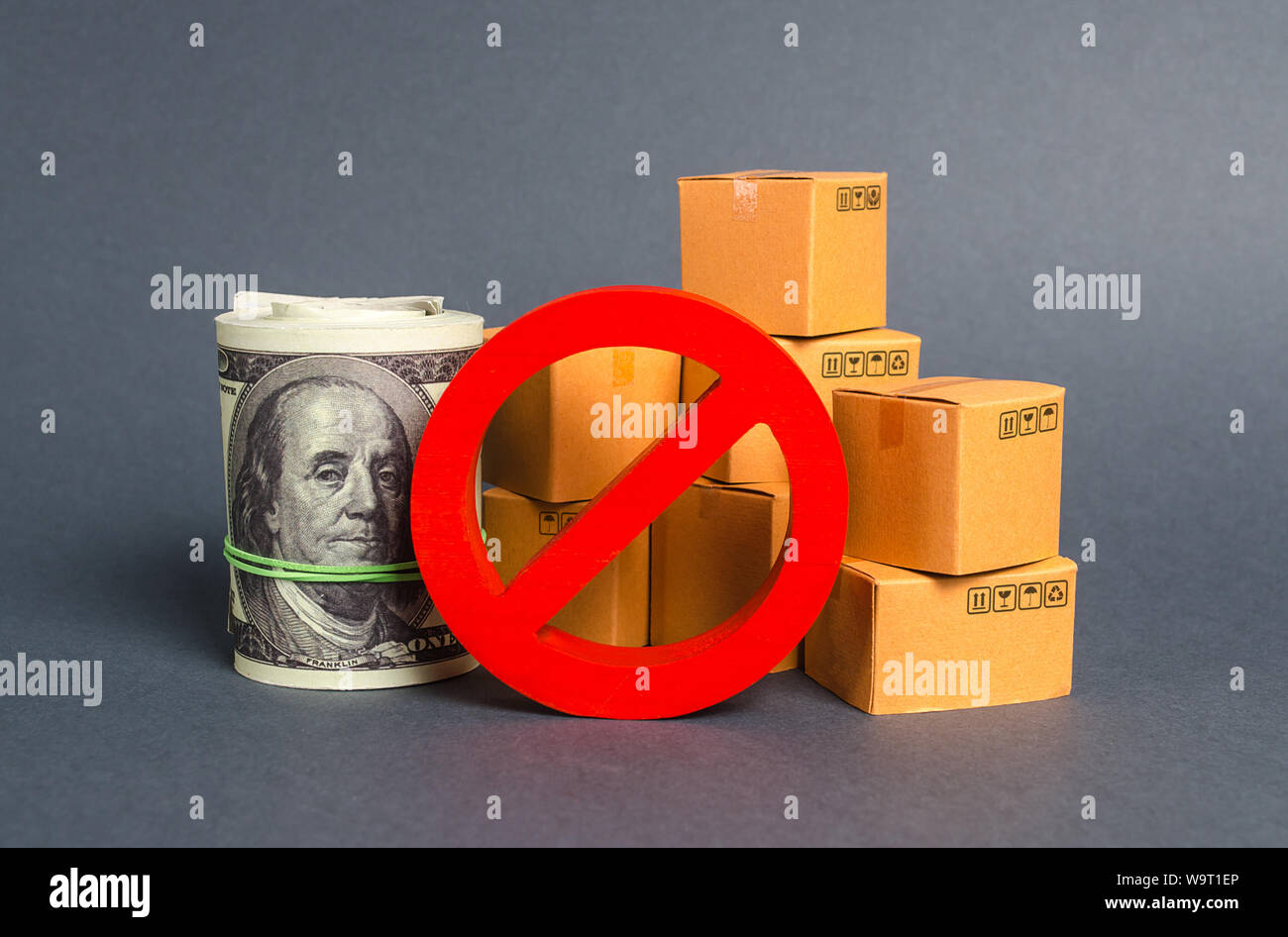The prohibition sign NO blocks a bundle of dollars money and cardboard boxes. Embargo, trade wars. Restriction on importation goods, proprietary for b Stock Photo
