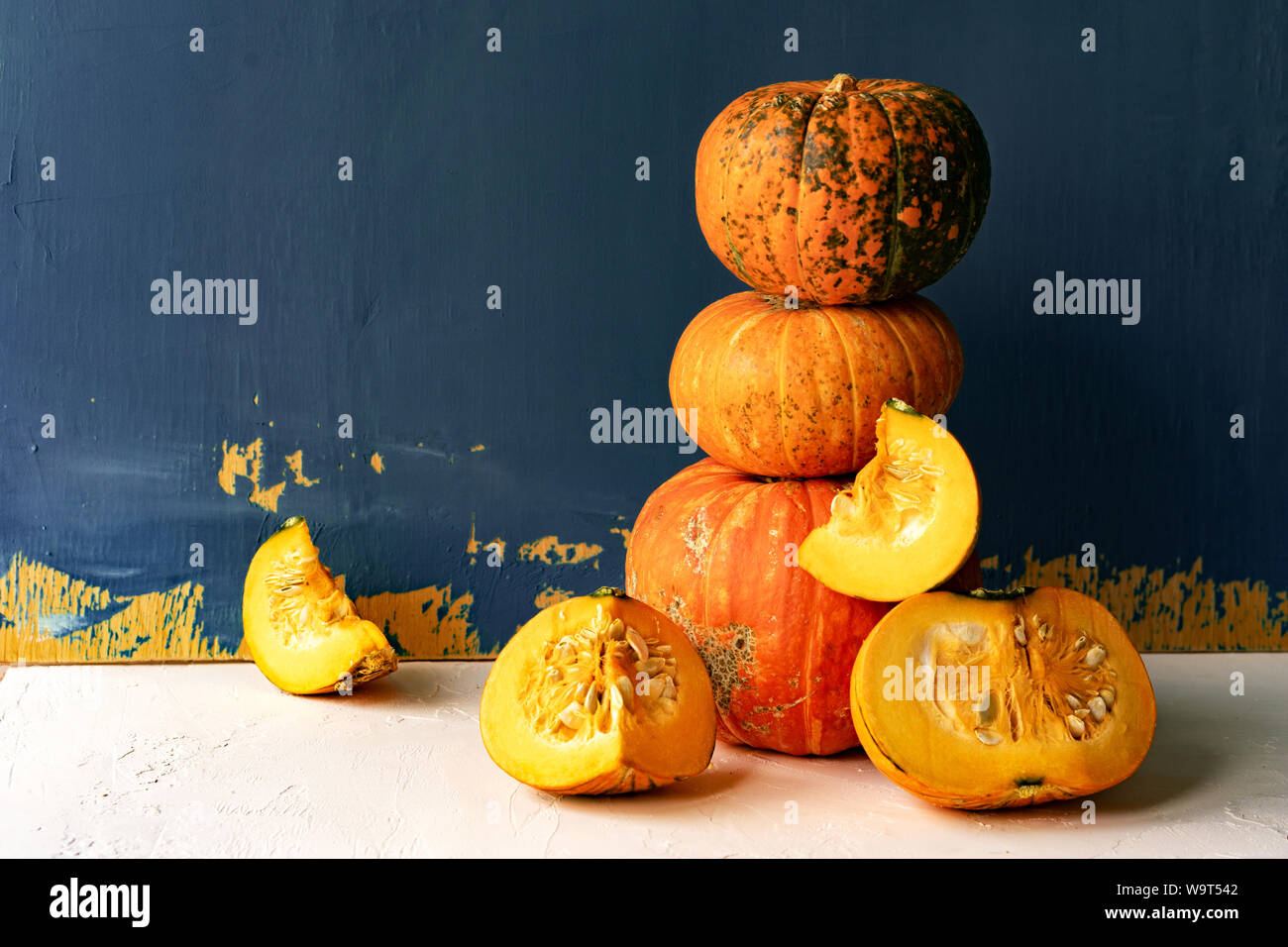 Large ripe pumpkins and cut pieces on a white concrete table against a painted blue wall Stock Photo