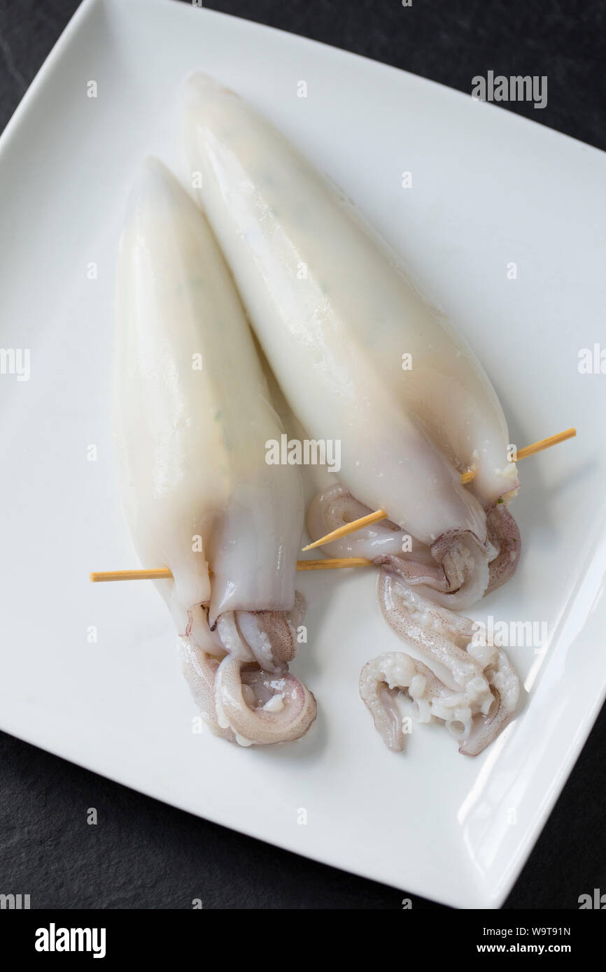 Two raw, prepared squid, Loligo vulgaris, that have been stuffed with scrambled egg other ingredients including parsley. The tentacles have been secur Stock Photo