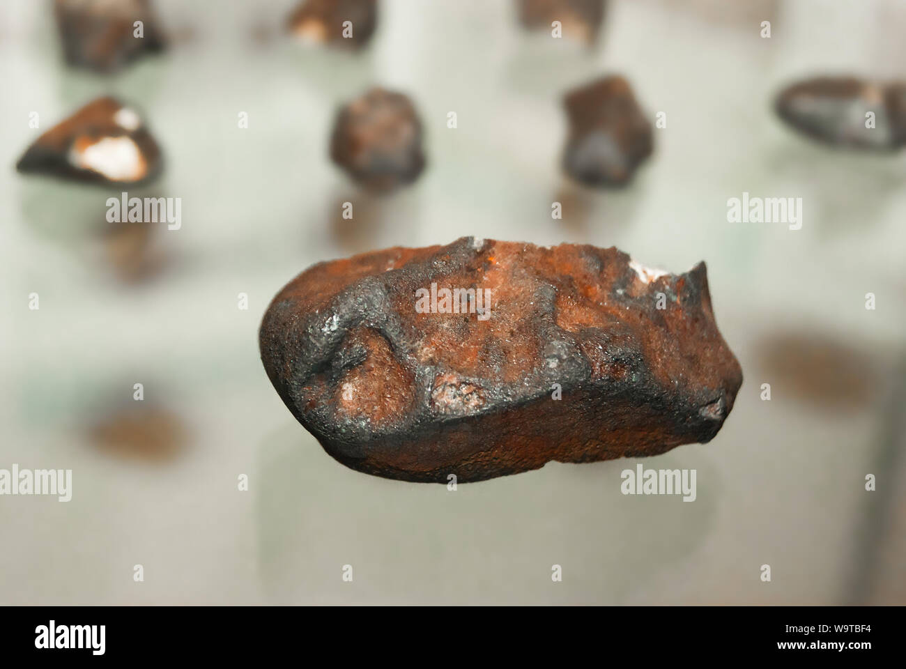 fragment of a meteorite on a glass showcase close up, against the background of other blurry fragments Stock Photo