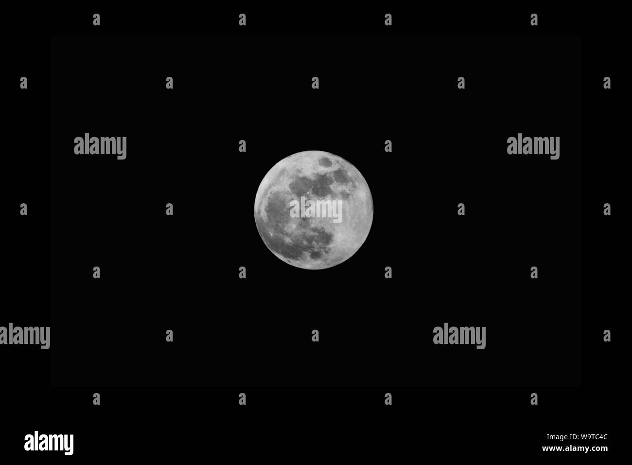 Grey full moon in the center in the pitch-black dark sky at night Stock Photo
