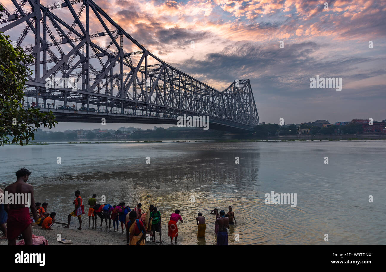 Silhouette of People , taking Holy bath in River Ganges overlokking the Howrah Bridge, a bridge with a suspended span over the Hooghly River in West B Stock Photo