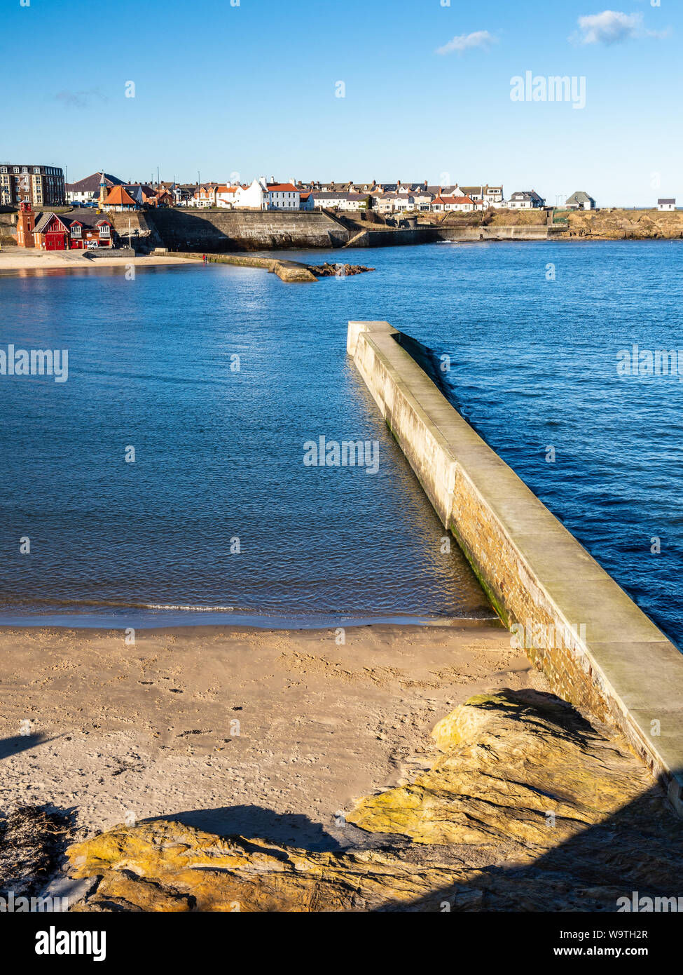 Sun shines on the harbour wall breakwaters and lifeboat station at Cullercoats Bay in Tyneside. Stock Photo