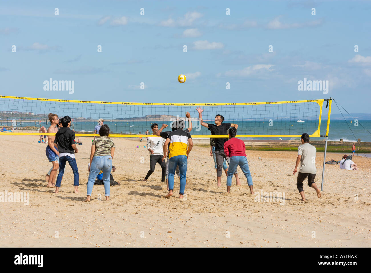 Bournemouth, UK. 15th August 2019, Weather: It’s a fickle British summer. Sunshine with a moderate breeze and temperature at a modest 20 degrees, a respite day before more wind and heavy rain arrives tomorrow. A group of young people play volleyball on the beach. Credit: Paul Biggins/Alamy Live Stock Photo