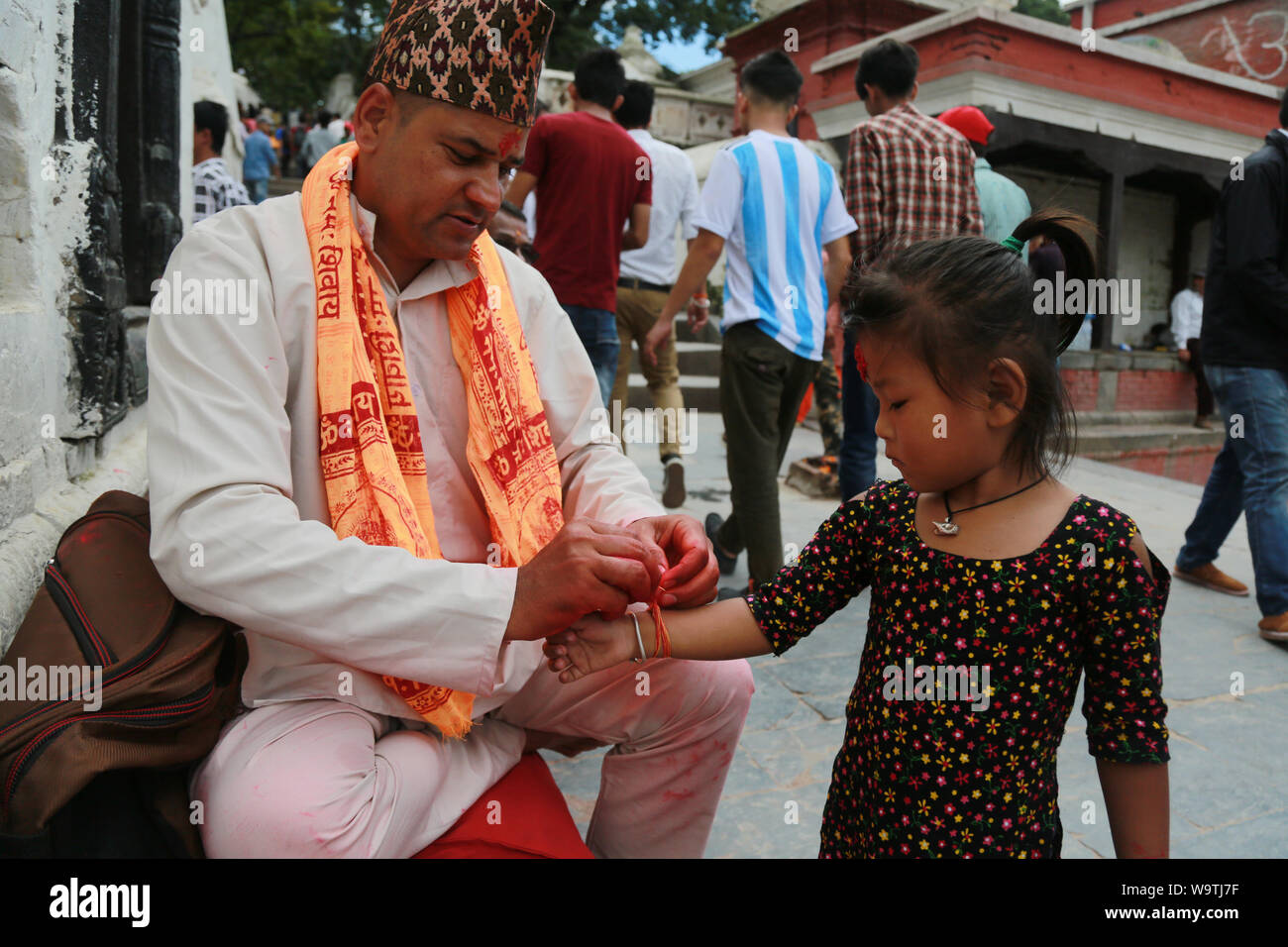 Kathmandu, Nepal. 15 August, 2019. Hindu Preist Tying the tread to young girl at Pashupatinath Temple. Sarita Khadka/Alamy Live News Stock Photo