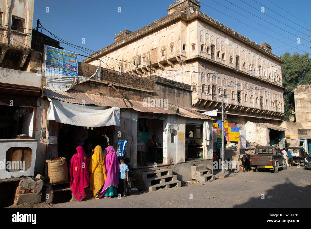 Eine Straße mit einem alten Haveli, einer Schneiderei und drei Frauen in bunten Saris beim Einkaufen Stock Photo
