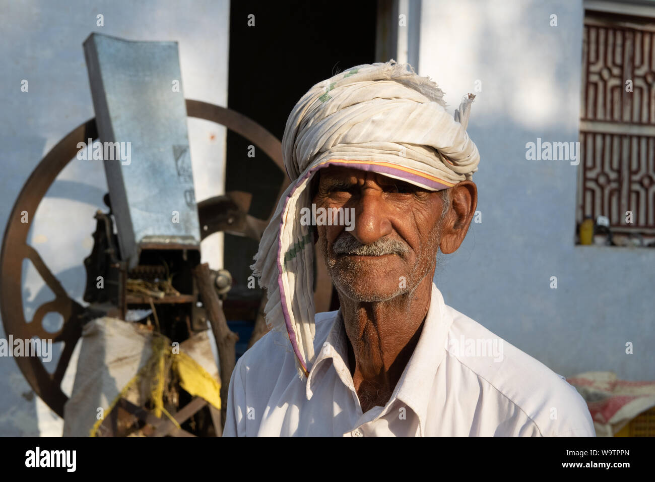 Ein alter Mann sitzt in einem Hof vor seinem Haus. Auf dem Kopf trägt er ein Tuch (Turban). Straßenszene in Mandawa (Rajasthan) Stock Photo