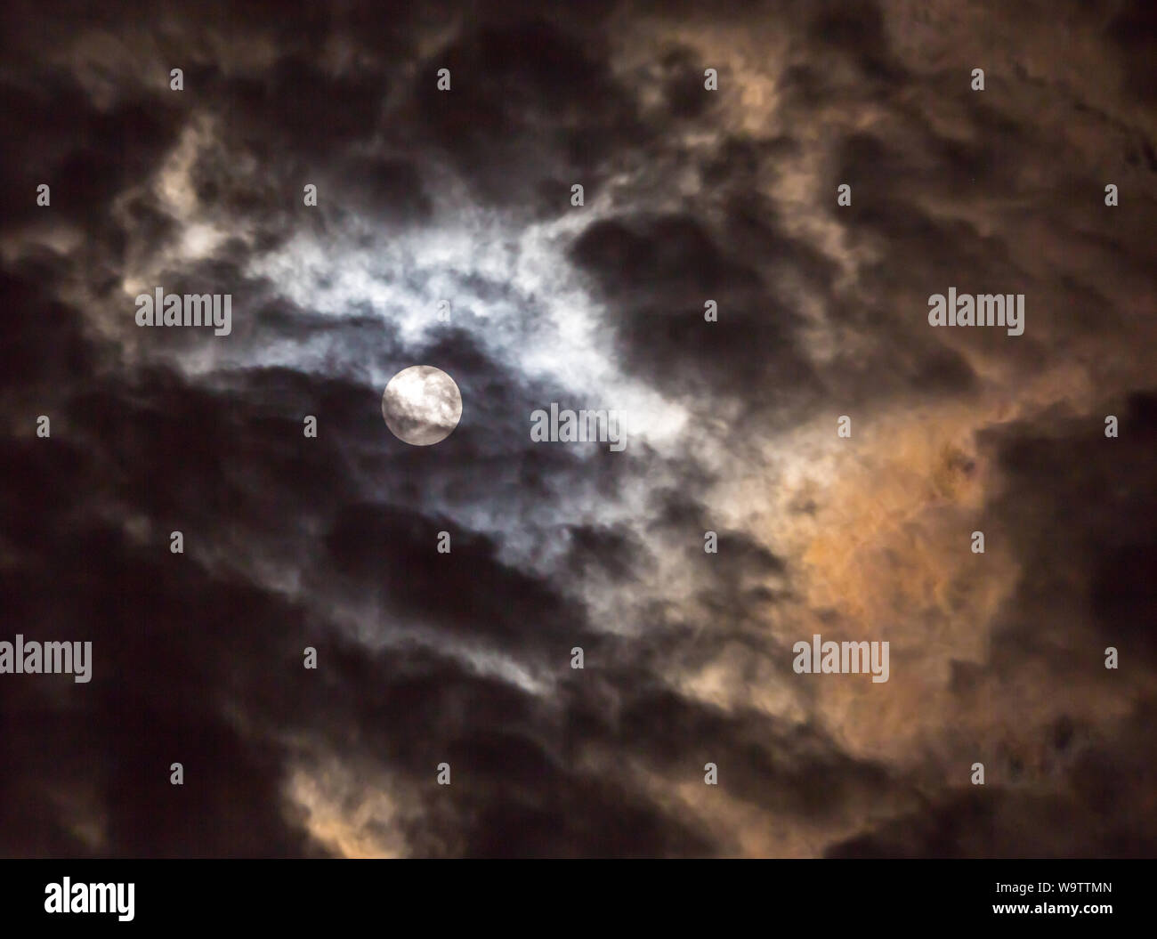 The glow of a full moon dramatically lights clouds in a night sky Stock ...