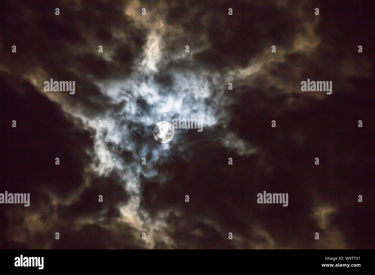 The glow of a full moon dramatically lights clouds in a night sky Stock