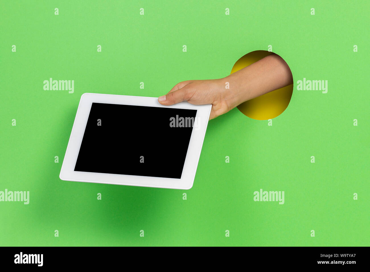 Kid holding tablet computer in hand through hole on light green background Stock Photo