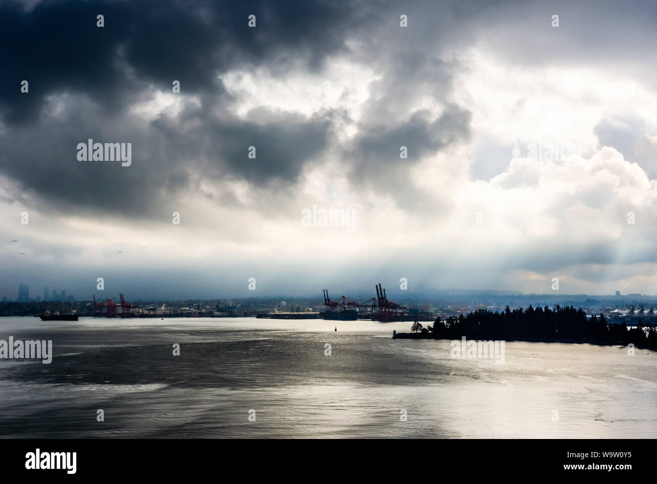 Sun breaking through from behind dark clouds in high contrast over water in Vancouver, British Columbia, Canada. Stock Photo