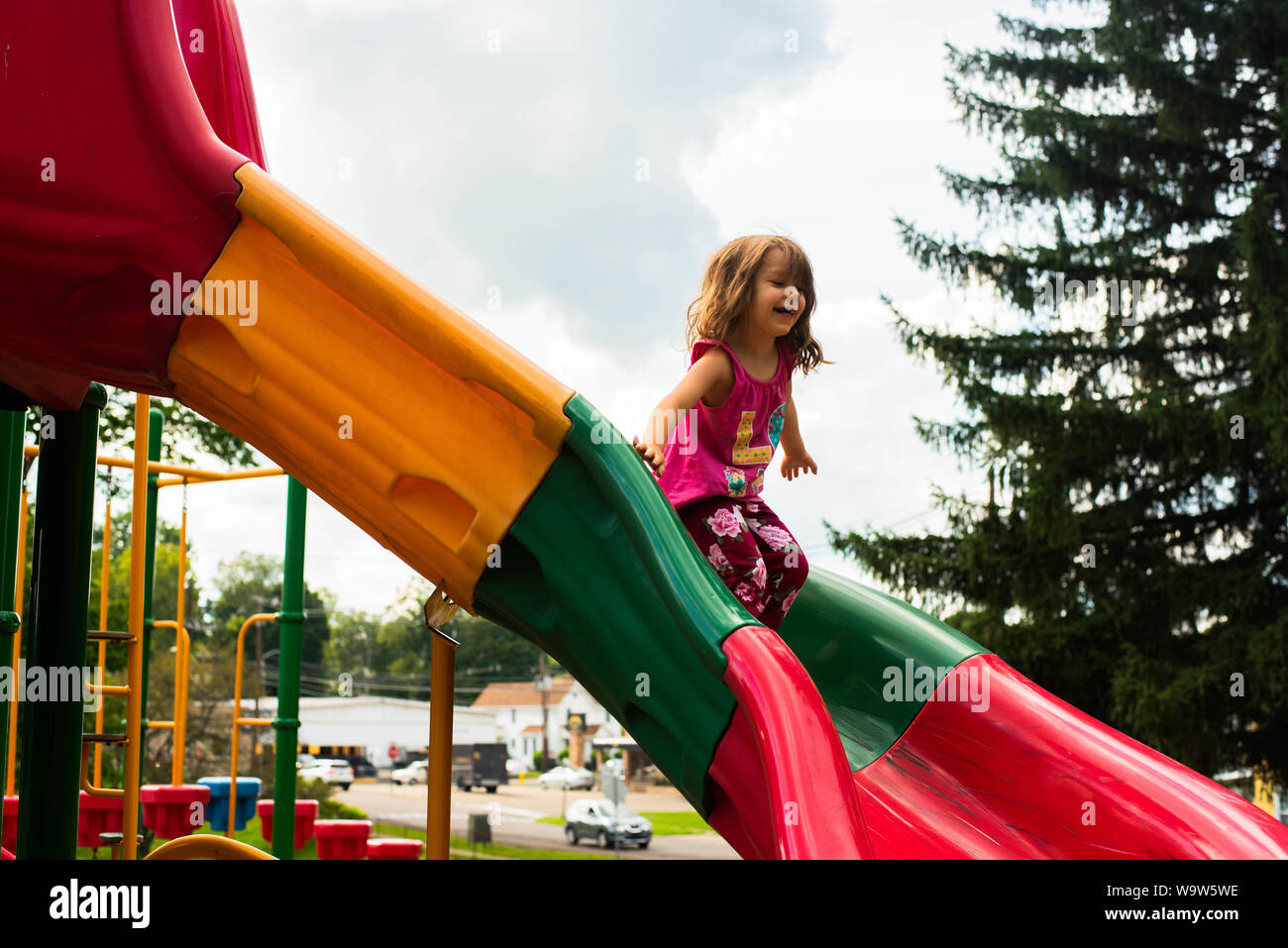 A 4-year old girl on a colorful slide on a playground. Stock Photo