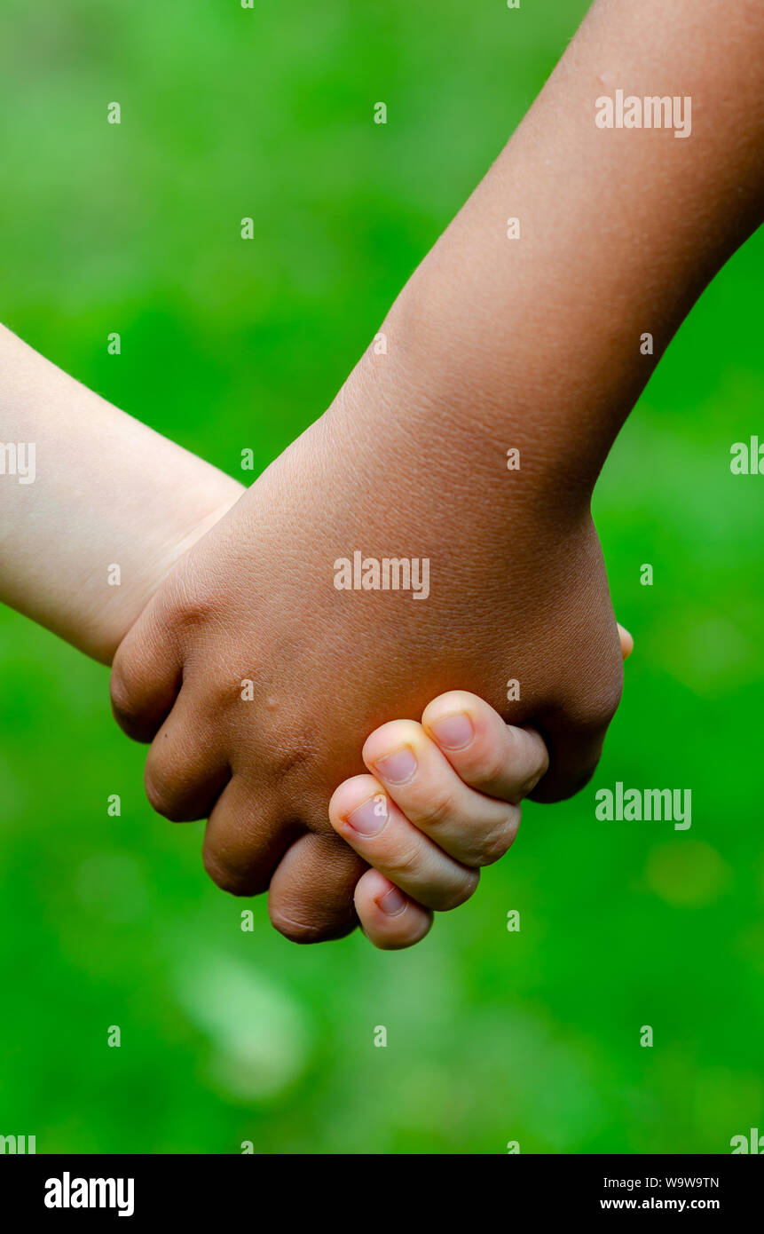 Boy and girl of different races hold hands together. Boy is Caucasian (white) and the girl is black. Concept for friendship, peace, support, equality. Stock Photo
