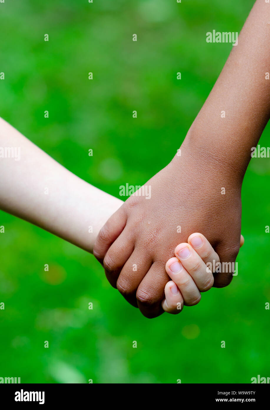 Boy and girl of different races hold hands together. Boy is Caucasian (white) and the girl is black. Concept for friendship, peace, support, equality. Stock Photo