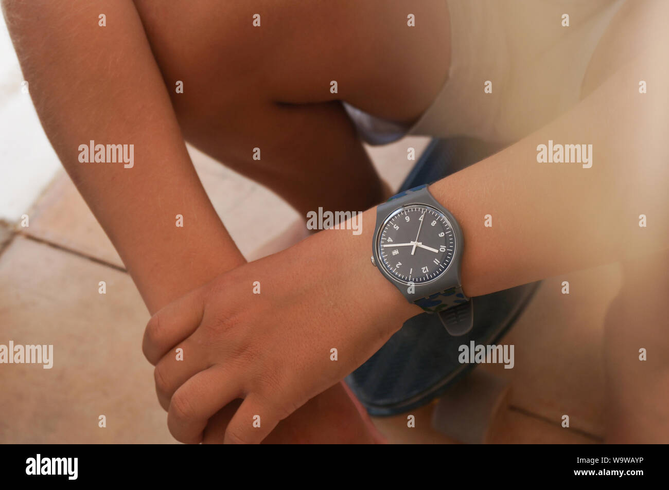 Alicante, Spain - August, 2019: Blue rubber Swatch watch on teenager's wrist sitting on skate board Stock Photo