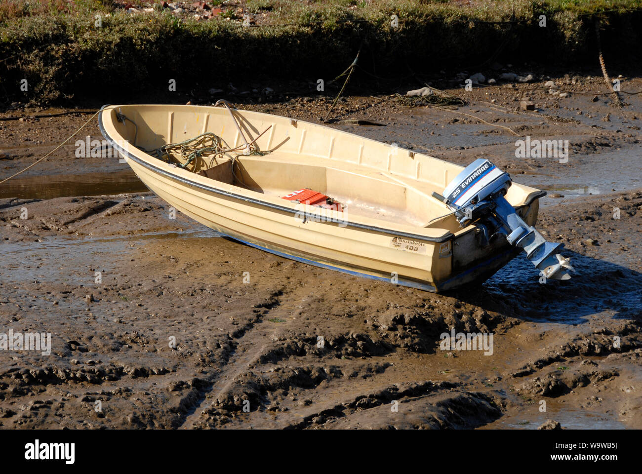 Small boat, marked 'Unsinkable' and with Evinrude outboard engine, stranded on the mud at Brancaster Staithe, on the north Norfolk coast, at low tide Stock Photo